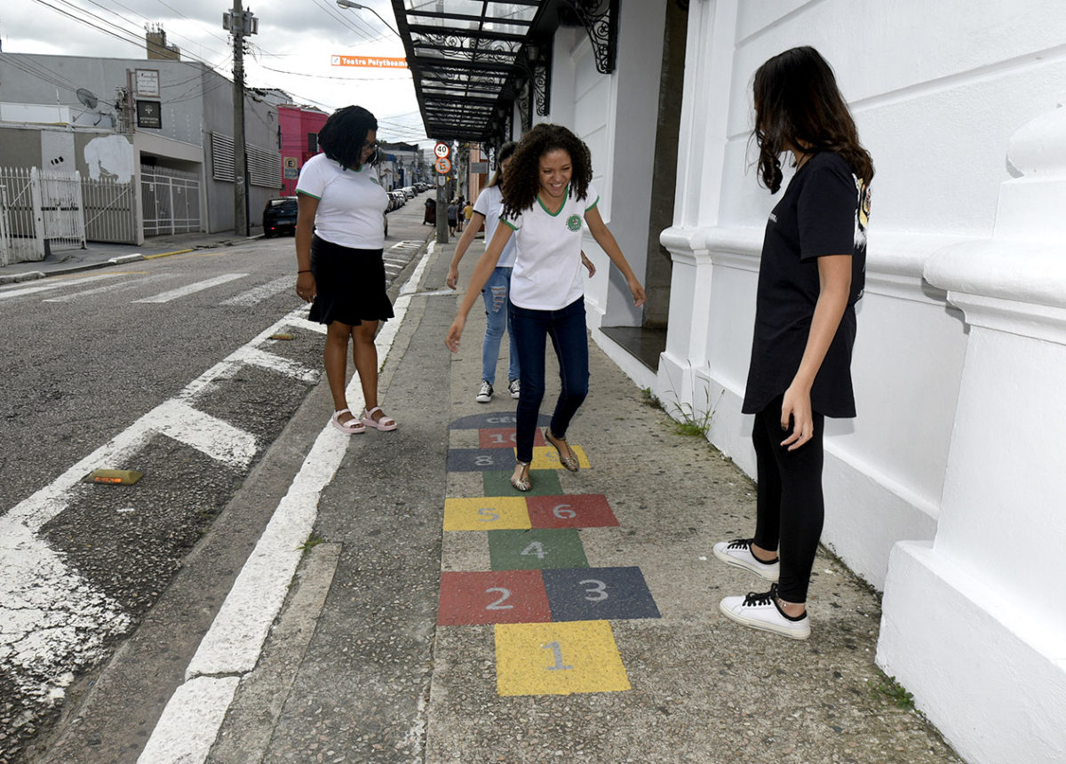 Quatro adolescentes brincando de pular amarelinha em frente ao Teatro Polytheama