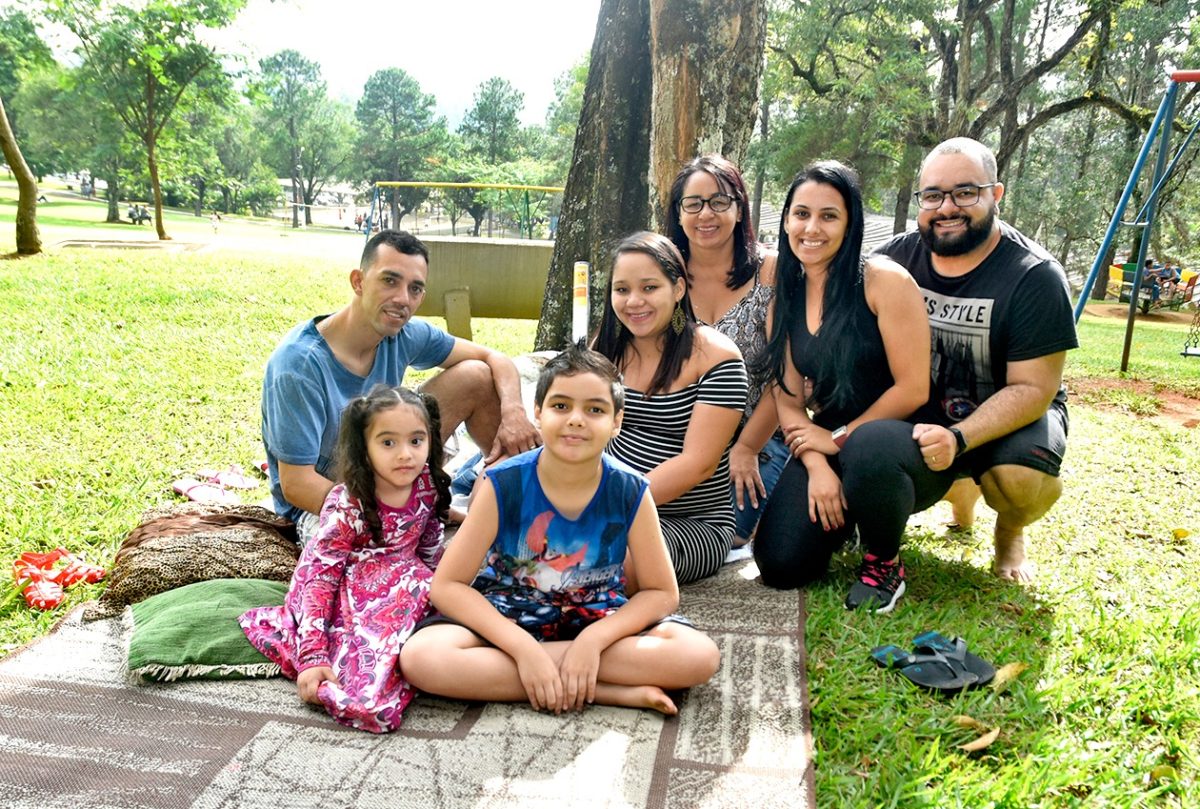 Família fazendo pic nic sobre gramado, em cima de toalha