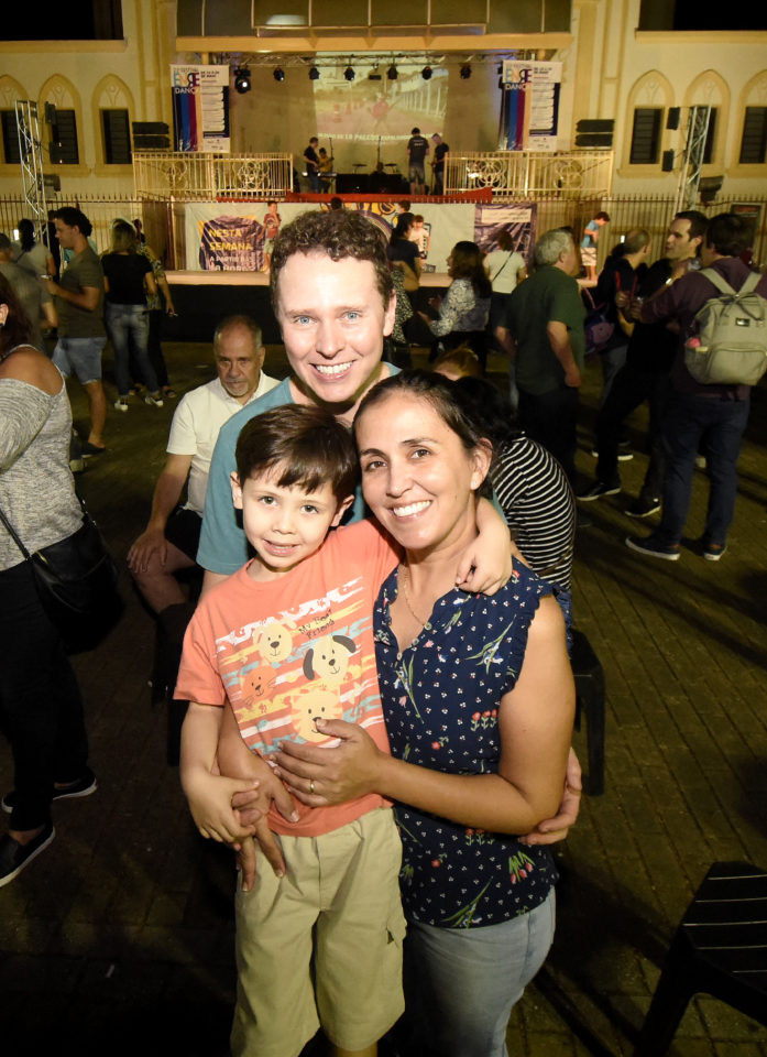 Casal e filho em foto posada, em pé, com os palcos montado e do Coreto e fundo da Matriz atrás, cercados de pessoas