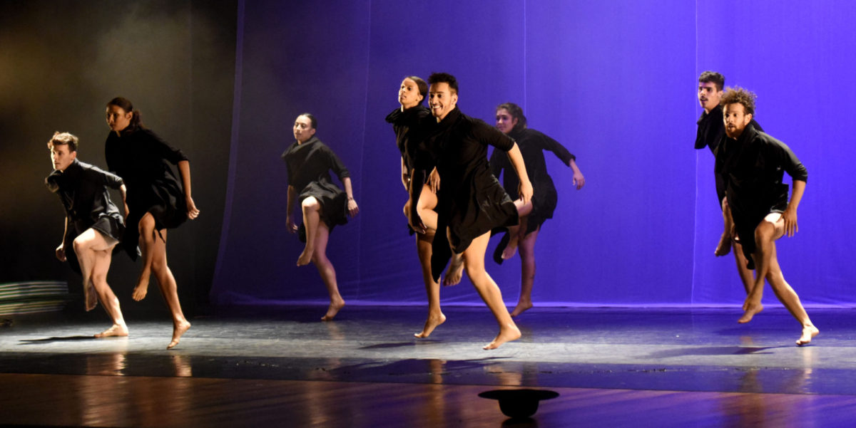 Bailarinos com figurino todo preto, em apresentação no palco do Polytheama, com luzes roxas ao fundo