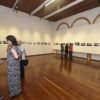 Salão de exposição da Pinacoteca com quadros e visitantes observando e conversando