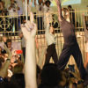 Bailarinos fazem performance de dança em grupo, com as mãos para o alto, m frente ao coreto, atrás da igreja Matriz