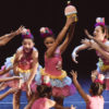Nove bailarinas infantojuvenis vestidas com fantasias de cupcakes em coreografia circular no palco