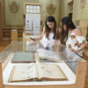 Duas moças olhando em redoma com documentos, em sala de exposições do Museu